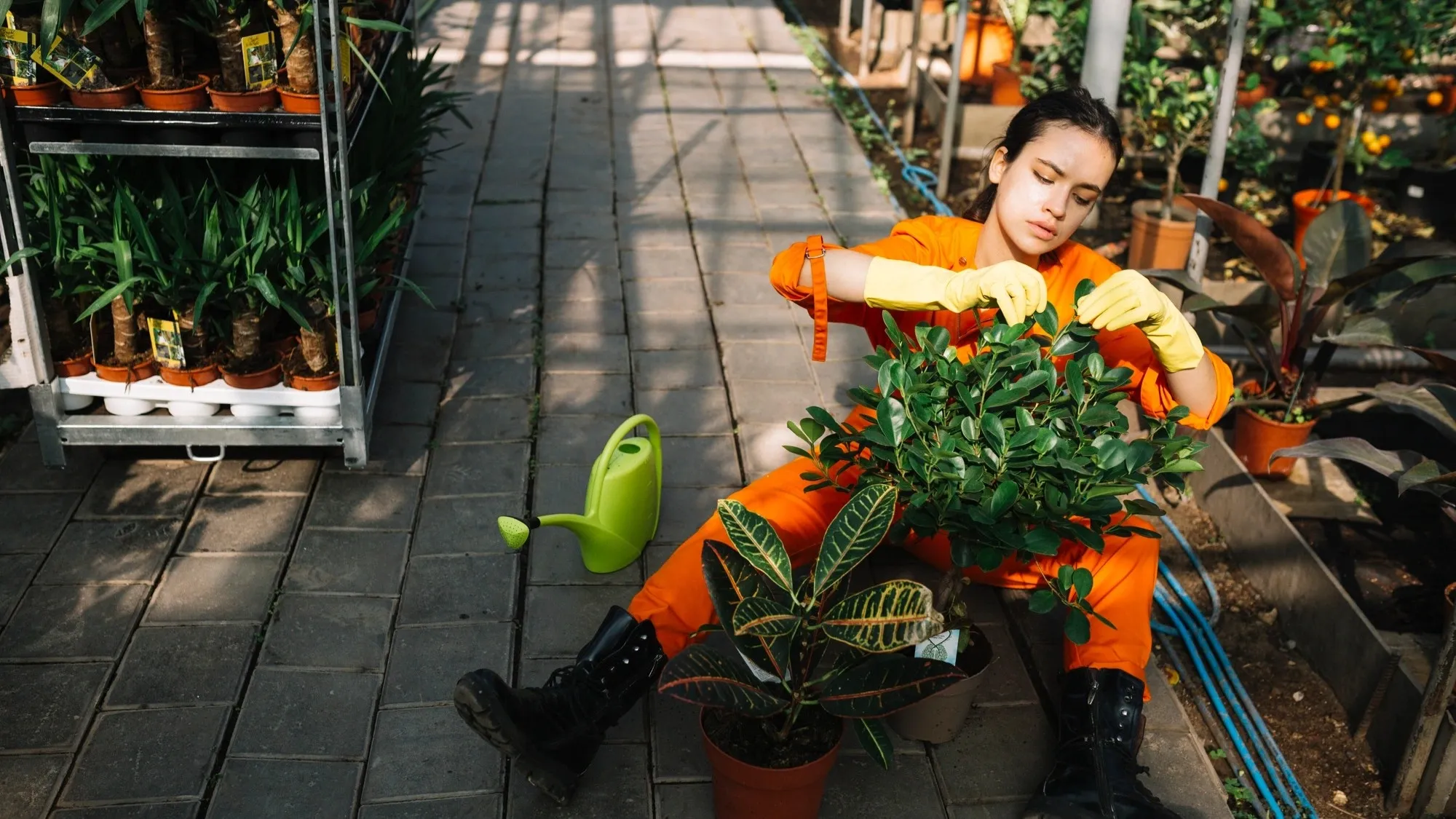 Wanita berkebun berjongkok di jalan setapak bata dengan gembor hijau